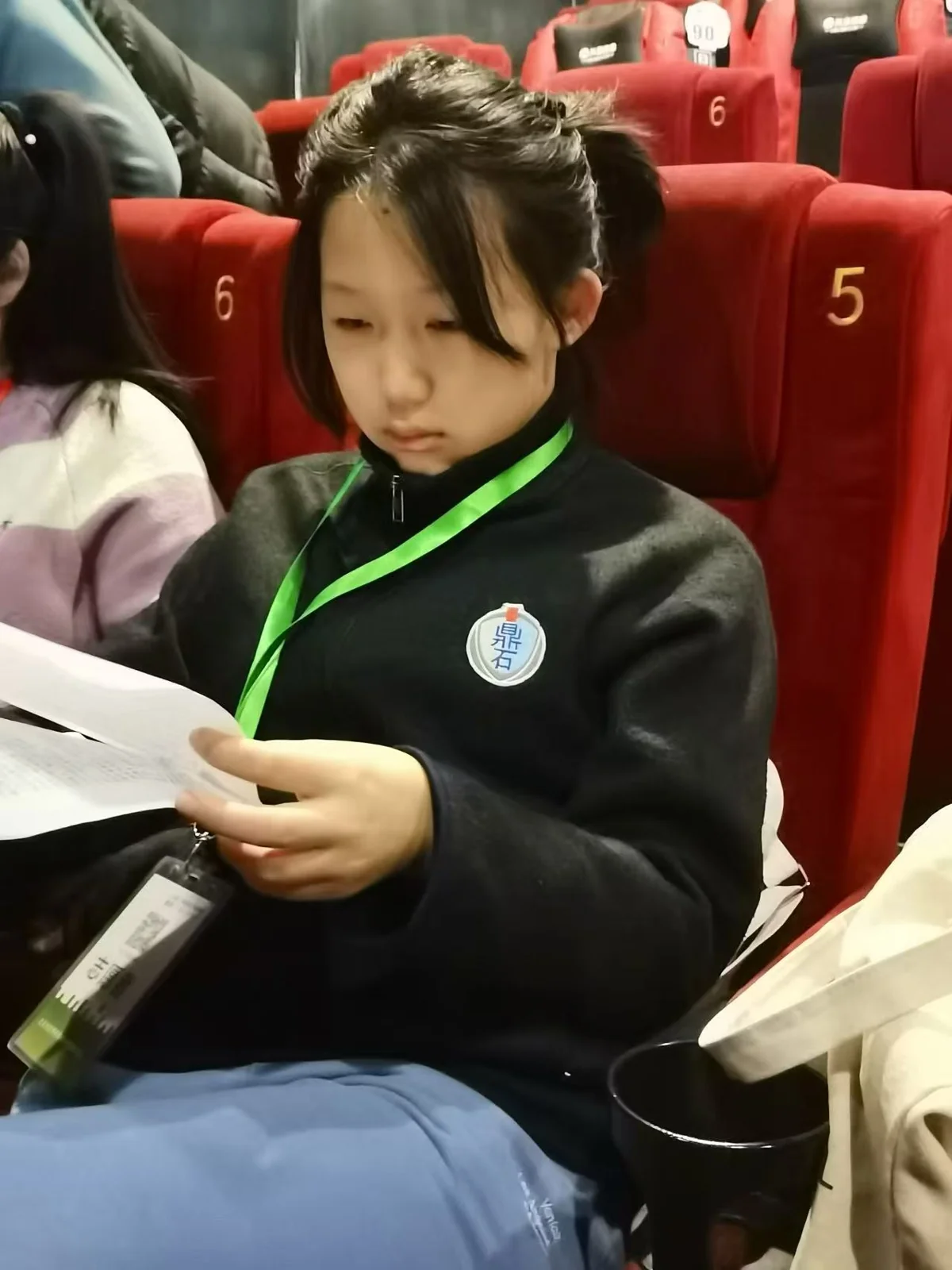 Liya reading from a printed script while seated in a cinema